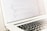 A close-up of a laptop displaying lines of HTML or programming code on its screen. The focus is on the code, with a shallow depth of field that blurs the background. The laptop is placed on a light-colored surface with its keyboard partially visible.