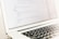 Close-up of hands coding on a laptop with construction plans nearby.