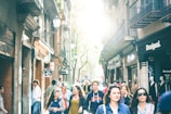 A bustling city street scene with people rushing past colorful storefronts under bright sunlight.