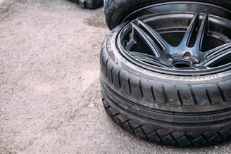A close-up of two stacked car tires with visible tread patterns. The surface beneath them appears to be rough and textured like concrete.