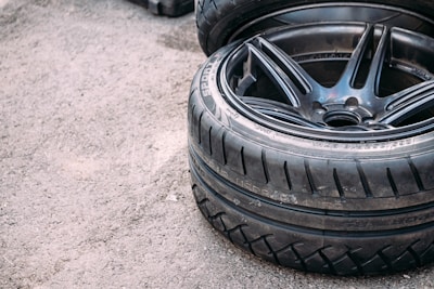 A close-up of two stacked car tires with visible tread patterns. The surface beneath them appears to be rough and textured like concrete.