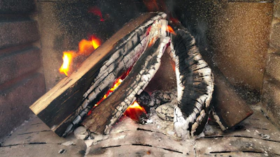 Close-up of bright orange flames flickering against dark wood in a cozy hearth.