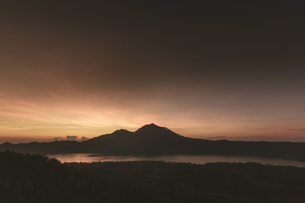 silhouette de montagne près du plan d’eau sous des nuages bruns