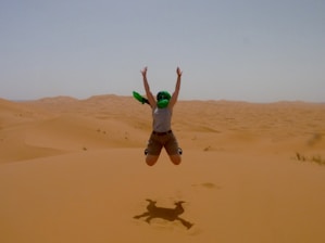 A person joyfully sandboarding down a steep golden dune under a clear blue sky.