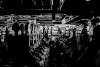 A dimly lit casino filled with rows of slot machines, some occupied by people. The machines' lights contrast with the dark surroundings, creating a vibrant yet subdued atmosphere.