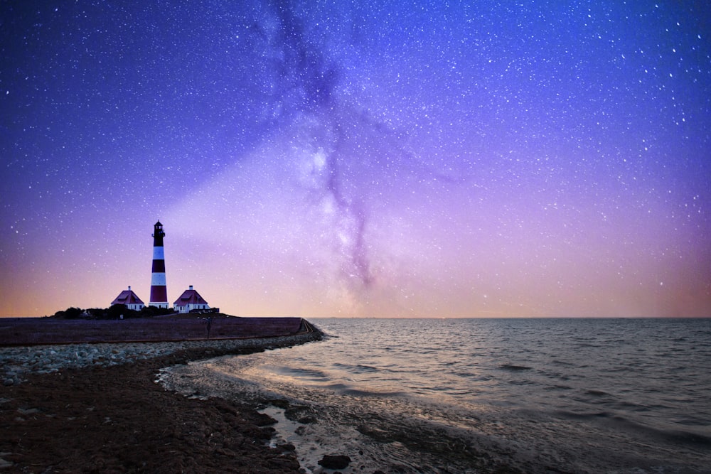 Faro blanco y rojo cerca de cuerpos de agua por la noche