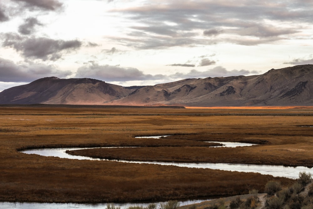 brown field near brown mountains under white clouds during daytime