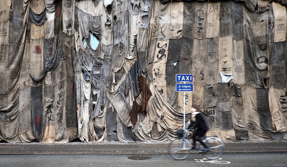 person riding bike on road beside cloth covered wall