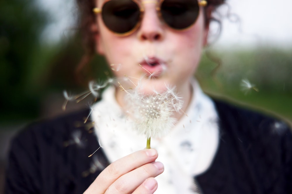 Frau bläst weiße Löwenzahnblüte