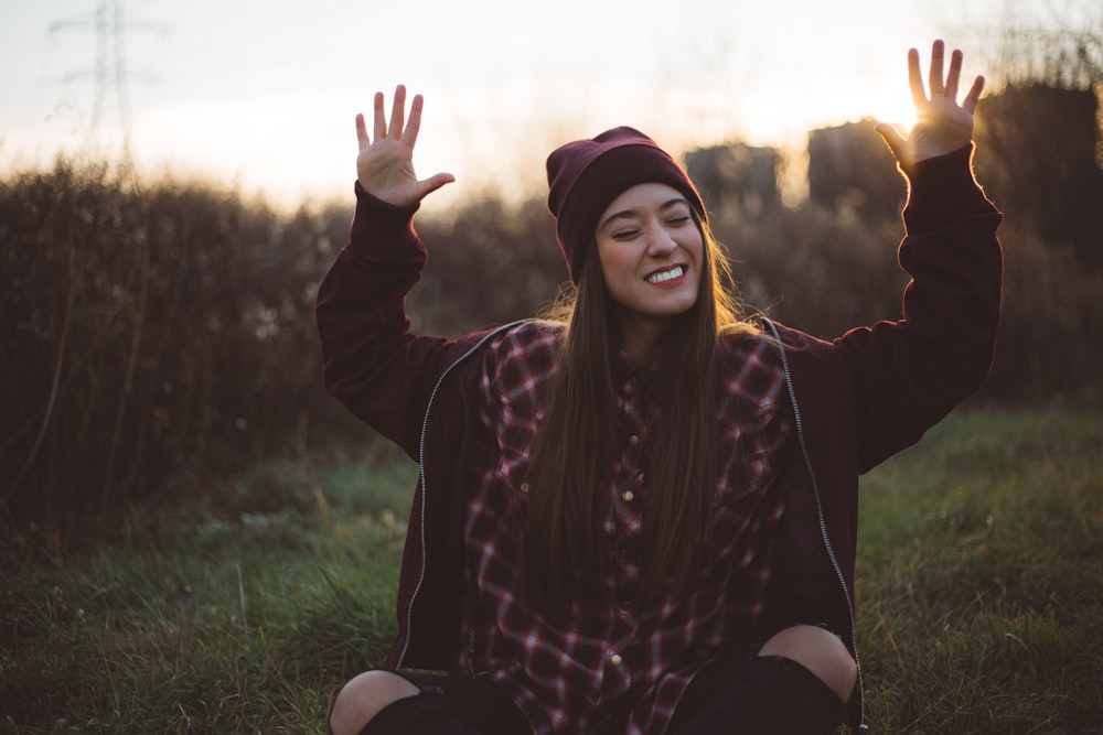 A happy woman sitting outside smiling with her hands raised to the sky.