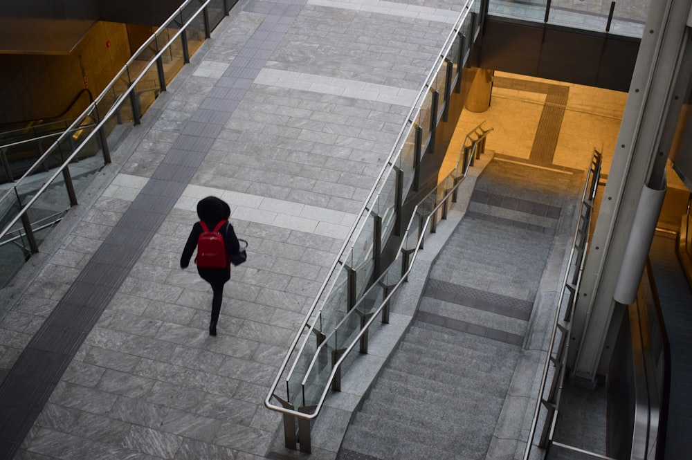 person in black hoodie with red backpack walking on walk bridge