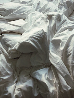 A shadowed, abstract close-up of crumpled linen softly lit to evoke an intimate, tactile atmosphere.