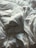 A close-up view of crumpled white bed sheets, creating an abstract pattern with various folds and creases. The fabric appears soft and the lighting casts gentle shadows, highlighting the texture.