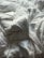 A close-up view of crumpled white bed sheets, creating an abstract pattern with various folds and creases. The fabric appears soft and the lighting casts gentle shadows, highlighting the texture.