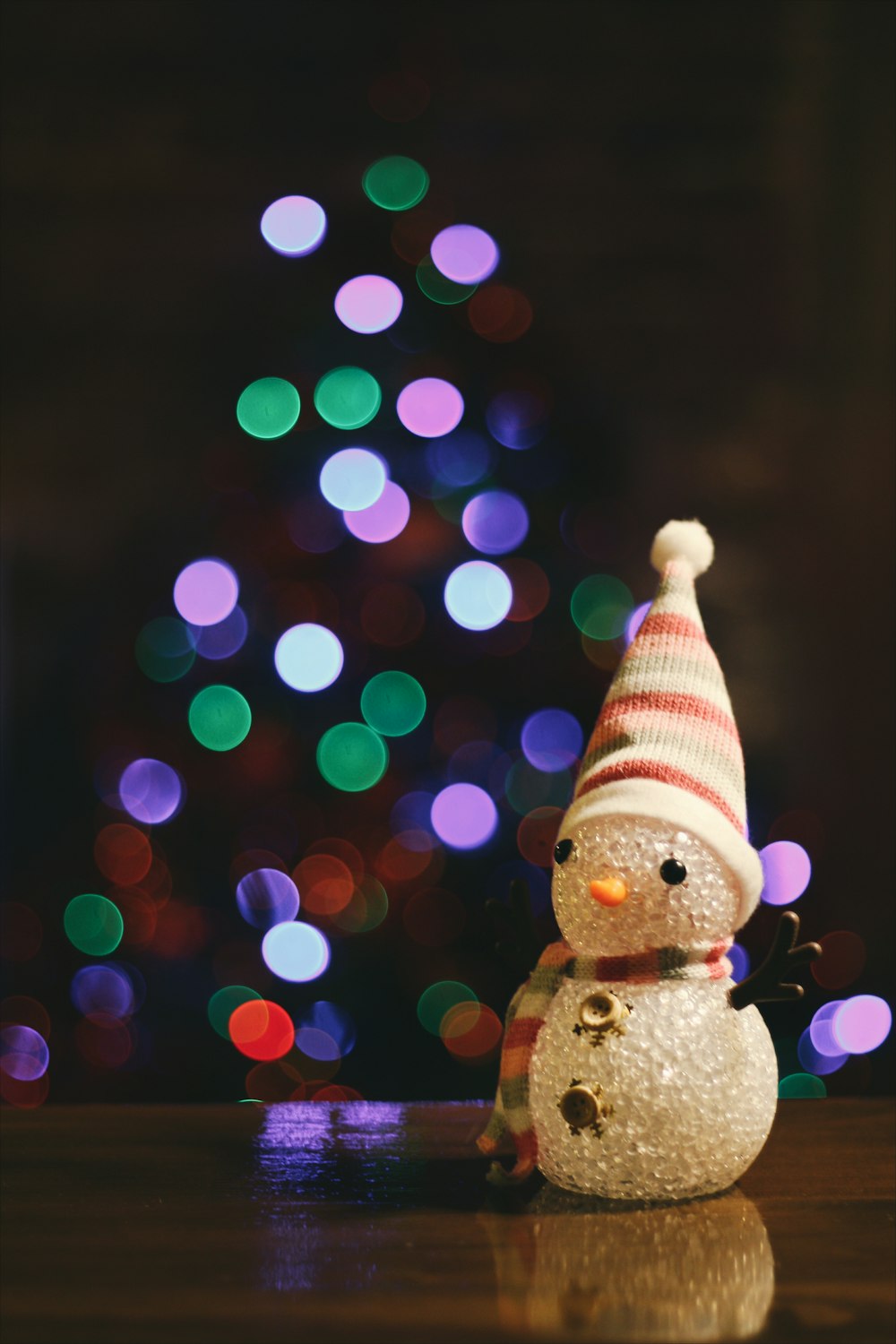 A little snowman figure sitting on the floor in front of a Christmas tree.