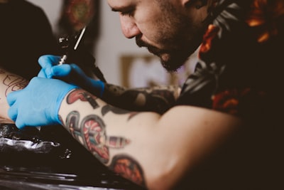 man doing tattoo on person's arm tattoo teams background