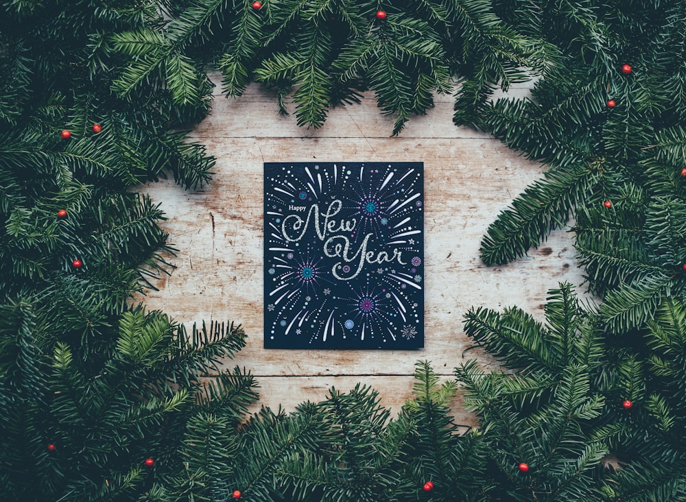 A wreath made of pine branches and holly surrounding a card that says Happy New Year