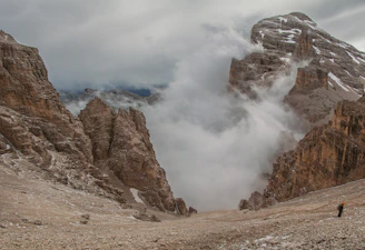 A dramatic mountain landscape at dawn with a lone hiker silhouetted against the sky.