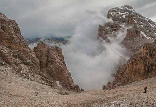 A dramatic mountain landscape at dawn with a lone hiker silhouetted against the sky.
