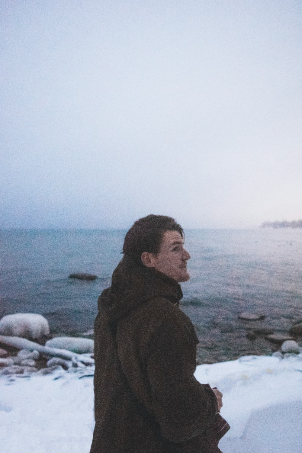 man in black hoodie standing on rocky shore during daytime