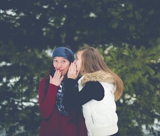 woman whispering on woman's ear while hands on lips