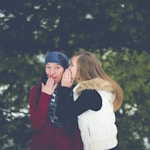woman whispering on woman's ear while hands on lips