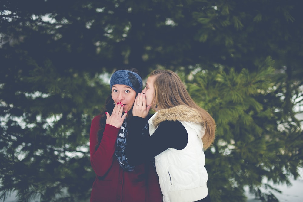 woman whispering on woman's ear while hands on lips