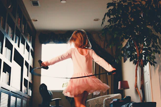 Smiling toddler girl twirling in a soft pink dress in a sunny room