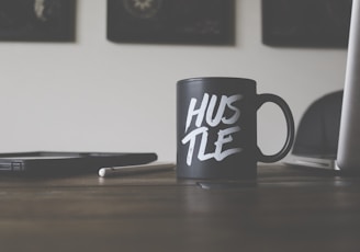 black and white Hustle-printed ceramic mug on table