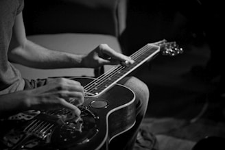 Close-up of hands skillfully playing a resonator guitar under moody blue lighting.