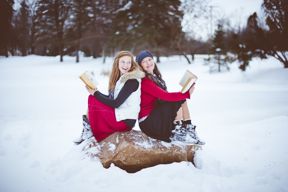 two women sitting on rock while holding books