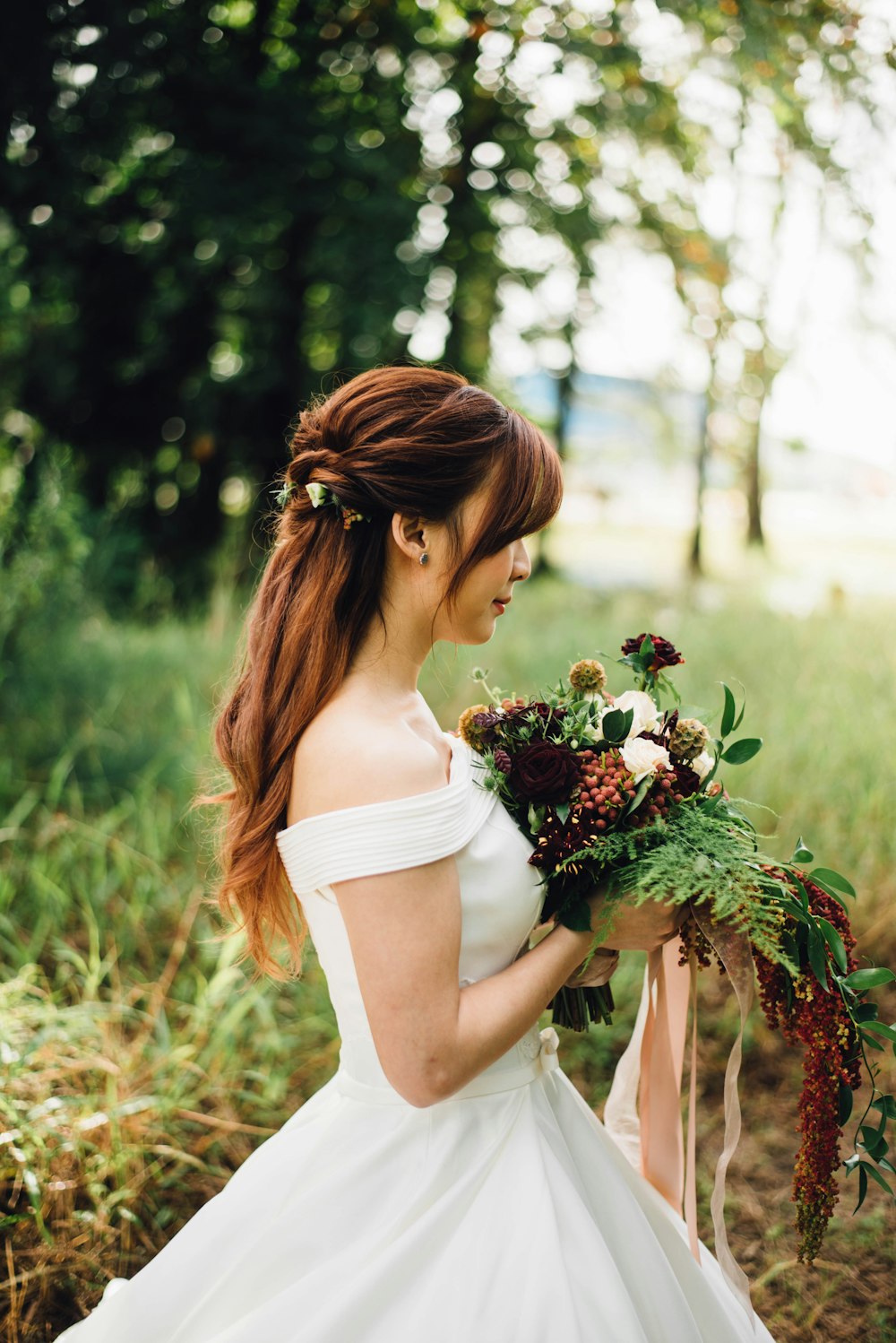 白いオフショルダーのウェディングドレスを着た女性は、白い花びらの花を身に着けています