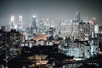 A bustling urban skyline at night showcasing a mix of modern skyscrapers and historic architecture lit up