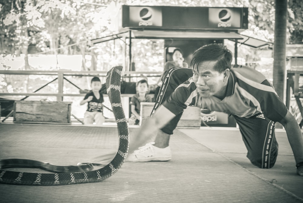 An Asian man playing with a snake on a sidewalk.