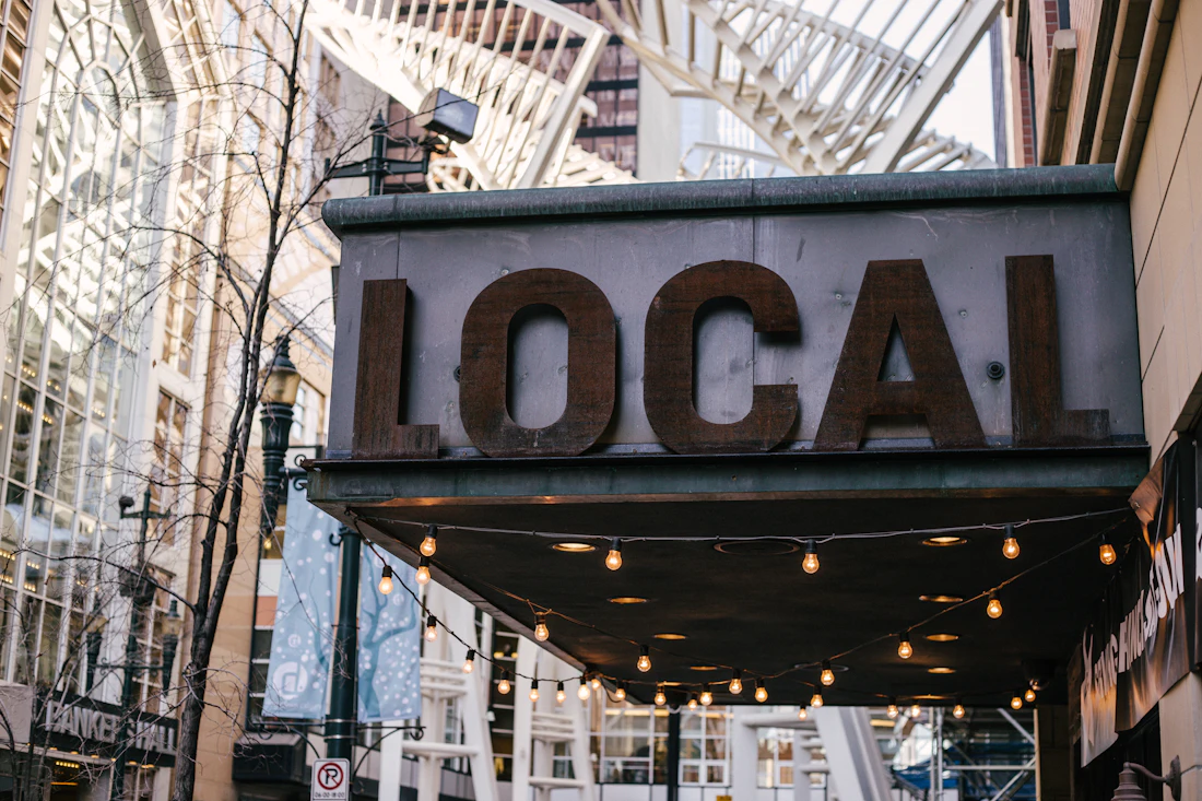 A weathered metal sign reading LOCAL above a shopfront awning strung with warm bulb lights