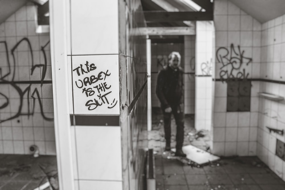 grayscale photo of man standing near white tile wall