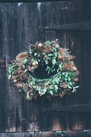 A colorful handmade wreath made from vibrant yarn and fabric scraps, hanging on a rustic wooden door.