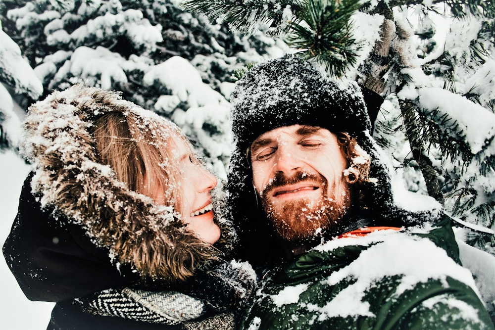 smiling man and woman standing under snow covered tree