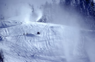 Snow making machines operating on a ski slope at dusk.