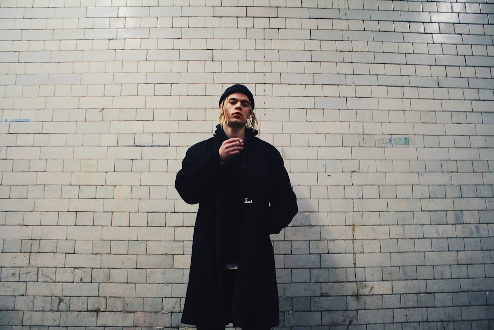 man standing near gray brick wall