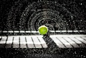 Close-up of a tennis ball hitting the racquet strings with water droplets flying in the air.