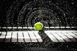 Close-up of a tennis ball hitting the racquet strings with water droplets flying in the air.