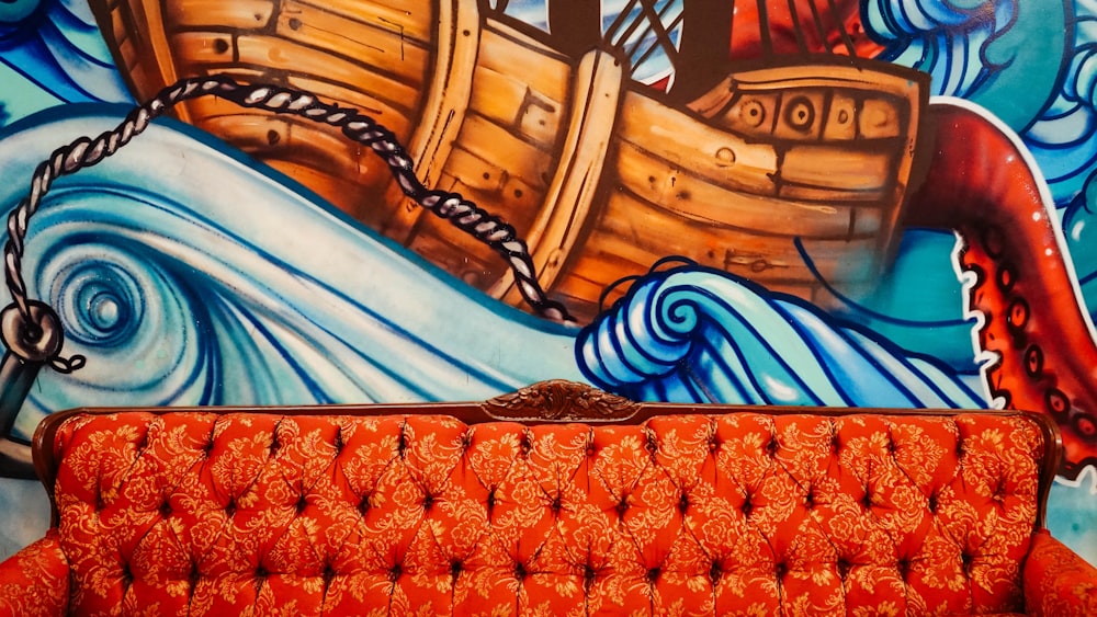 sofá laranja tufado com pintura mural de barco marrom na parte de trás