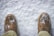 Brown leather shoes dusted with freshly fallen snow, positioned on a snowy ground. The surrounding snow appears clean and untouched, contrasting with the rugged texture of the shoes.