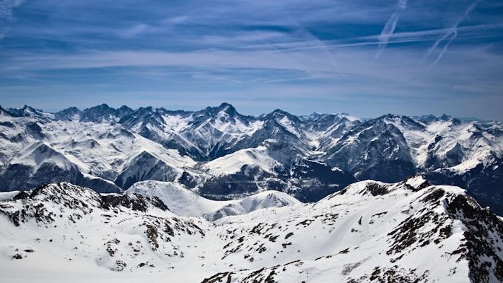 A panorama of snowy Oisans peaks seen from a high summit, with a skier's track in the foreground snow