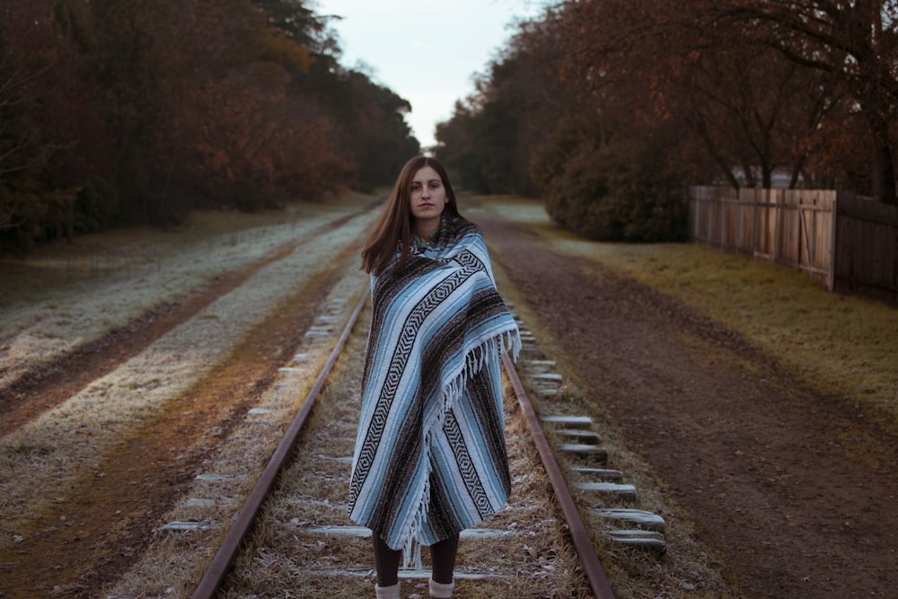 파란색과 검은색 줄무늬 스카프를 두른 여자가 낮에 갈색 기차 철도에 서 있다