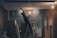 A person on a ladder is working on a ceiling, with a construction or renovation setting in the background. There are exposed light bulbs and various building materials scattered around. The lighting is low, casting shadows, and there is a misty or dusty atmosphere.