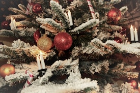 A Christmas tree adorned with a variety of festive decorations. Red and gold baubles hang from the snowy branches, while traditional candles illuminate the scene. Candy cane ornaments add a touch of sweetness to the holiday atmosphere.