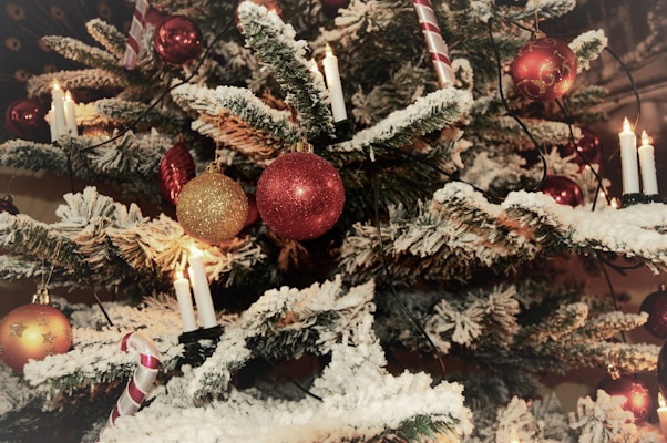 A Christmas tree adorned with a variety of festive decorations. Red and gold baubles hang from the snowy branches, while traditional candles illuminate the scene. Candy cane ornaments add a touch of sweetness to the holiday atmosphere.