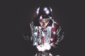 Close-up of a black oversized hoodie with vivid neon purple embroidered fantasy motifs glowing softly under dim light.